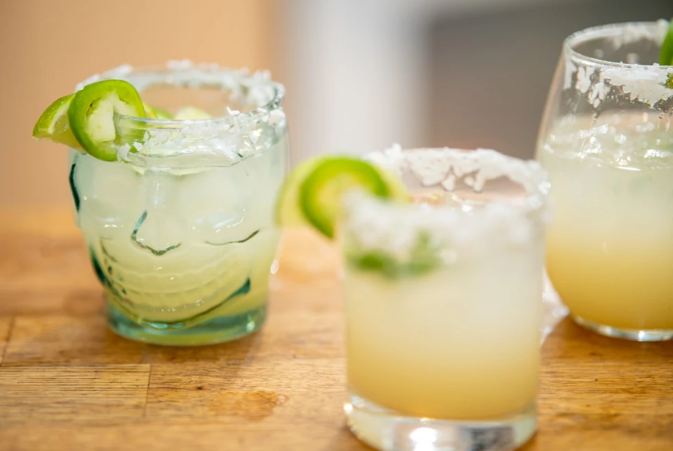 three margaritas with salt rim in a skill glass with jalapeño and lime on a wooden table