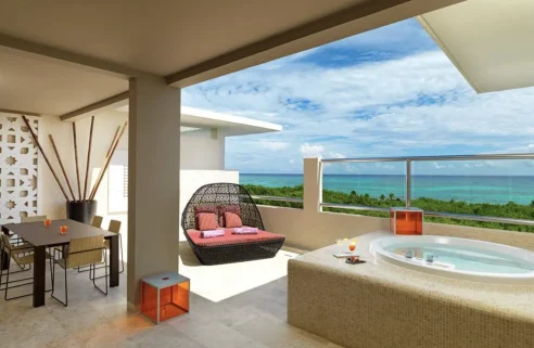 A patio at the Paradisus Playa del Carmen with a jacuzzi, table and lounge bed overlooking the ocean.