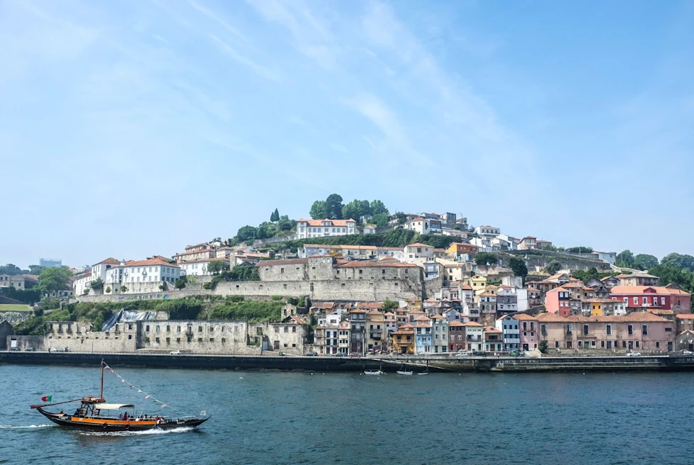 view of a town on a hill across a river with an old boat sailing past during the day