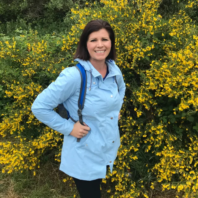 Travel Advisor Sarah Henderson in a blue jacket in front of a bush with yellow flowers.