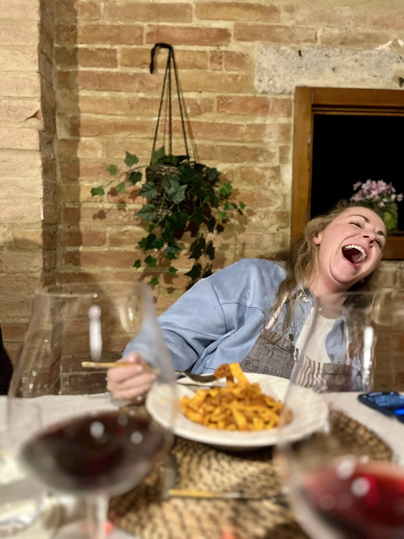 a woman laughs as she eats a bowl of pasta