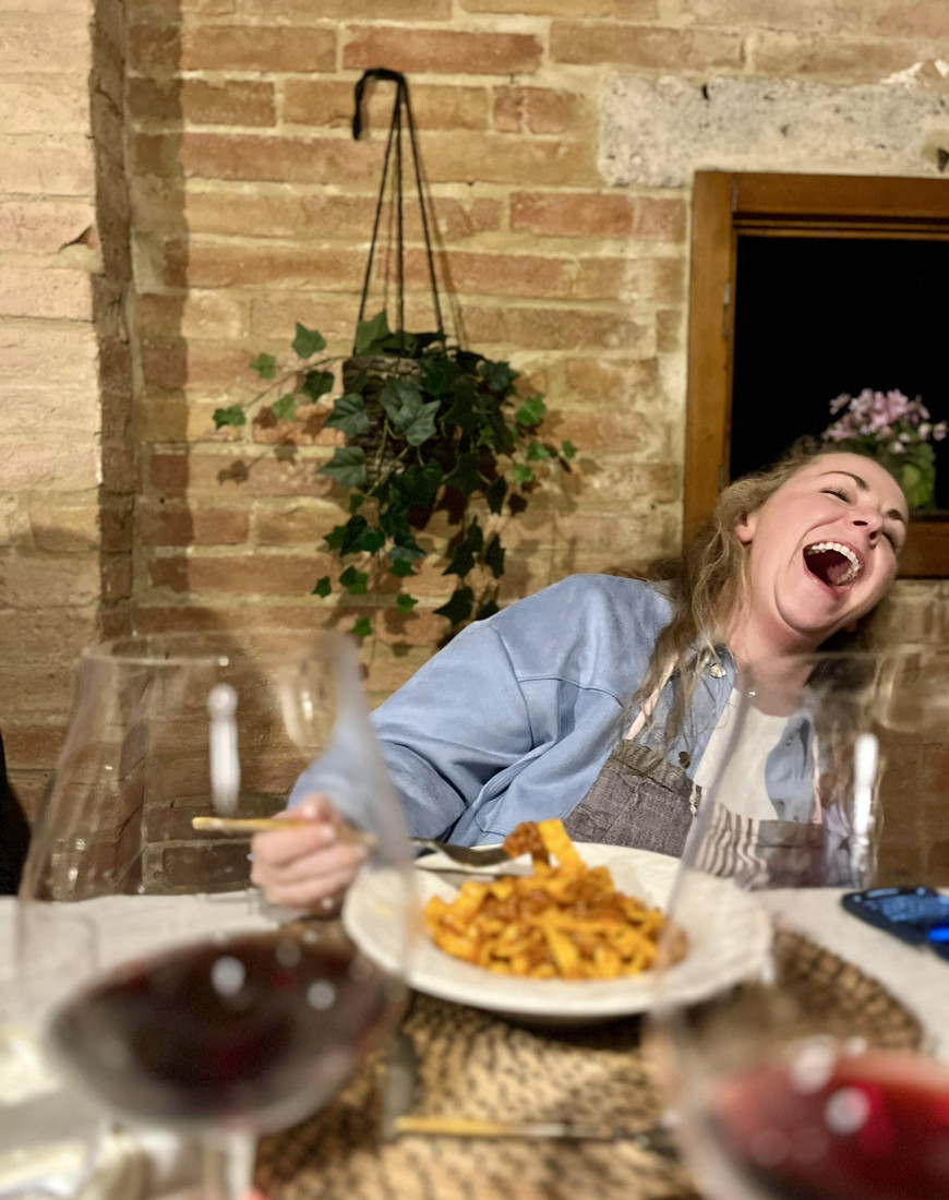 a woman laughs as she eats a bowl of pasta