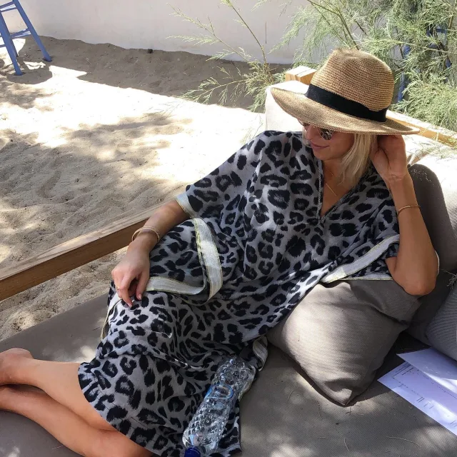 Travel Advisor Amanda Jay in a black and white leopard dress with  a beach hat sitting outside. 