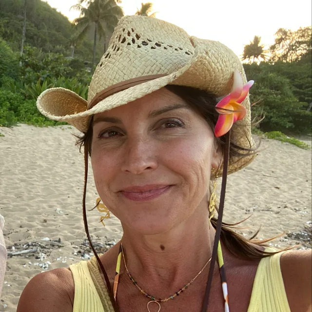 Travel Advisor Stephanie Culen with a cowboy hat on, pink flower in hair and a yellow shirt on a beach.