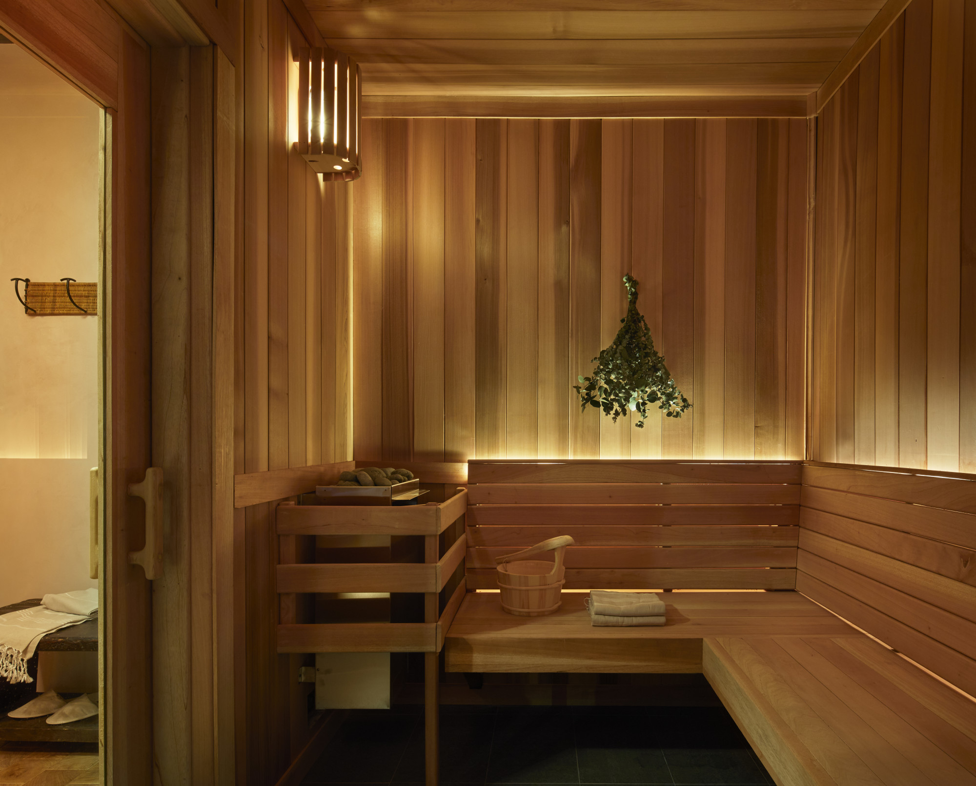 a bundle of green branches hangs in a sleek wooden sauna