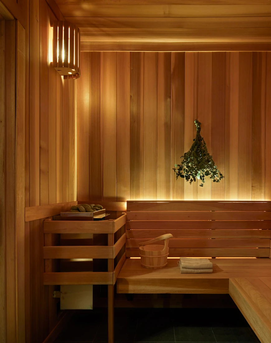 a bundle of green branches hangs in a sleek wooden sauna