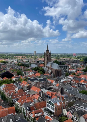A view of the Nieuwe Kerk tower surrounded by red-roofed buildings and a cloudy blue sky.