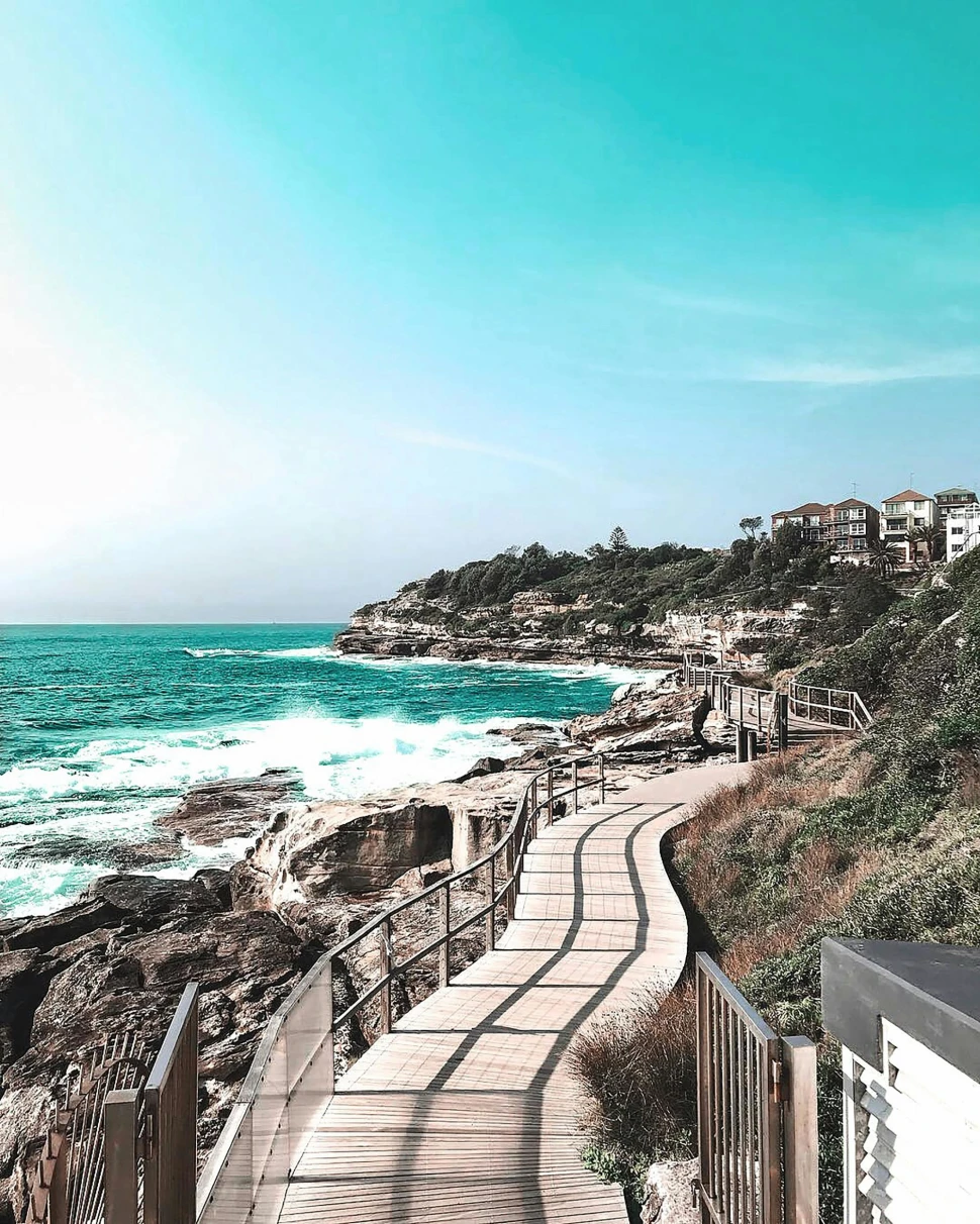A picturesque coastal pathway offering a view of the azure sea and rugged shores beneath a clear sky.