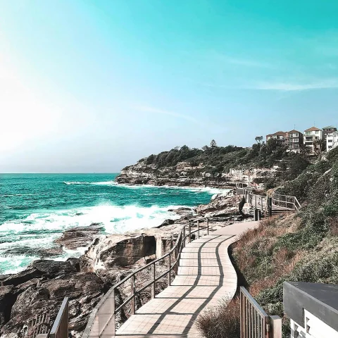 A picturesque coastal pathway offering a view of the azure sea and rugged shores beneath a clear sky.