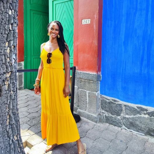 Travel Advisor Colette Gueye stands in front of a bright green and red door wearing a bright yellow dress