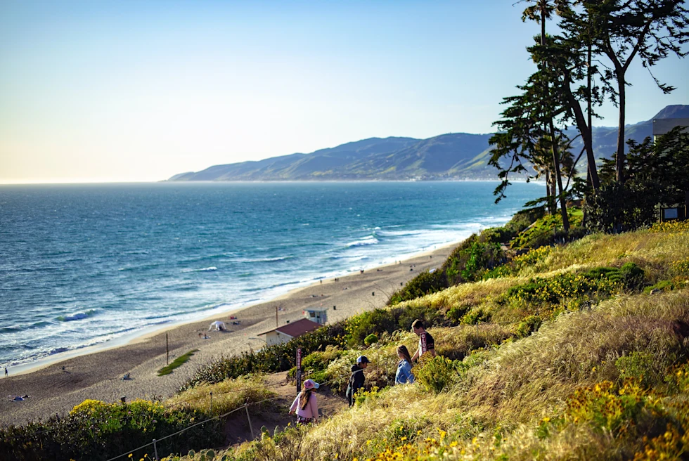 Beautiful blue water beach with people and green hills.