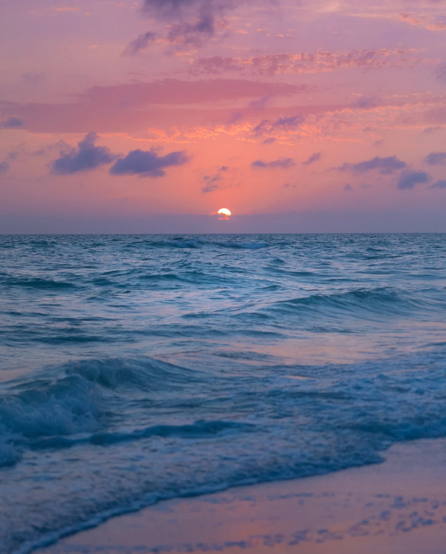 a final peak at the white sun during a pink and purple sunset over the ocean 