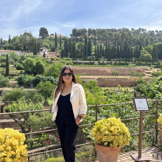 Woman wearing black pants and black top with trees and gardens in the background during daytime