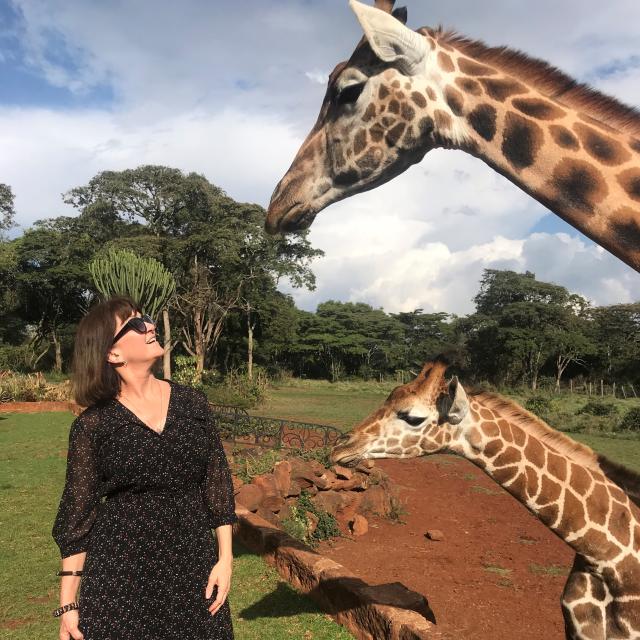 Fora travel agent Kara Kassuba wearing black dress and sunglasses and standing next to two giraffes