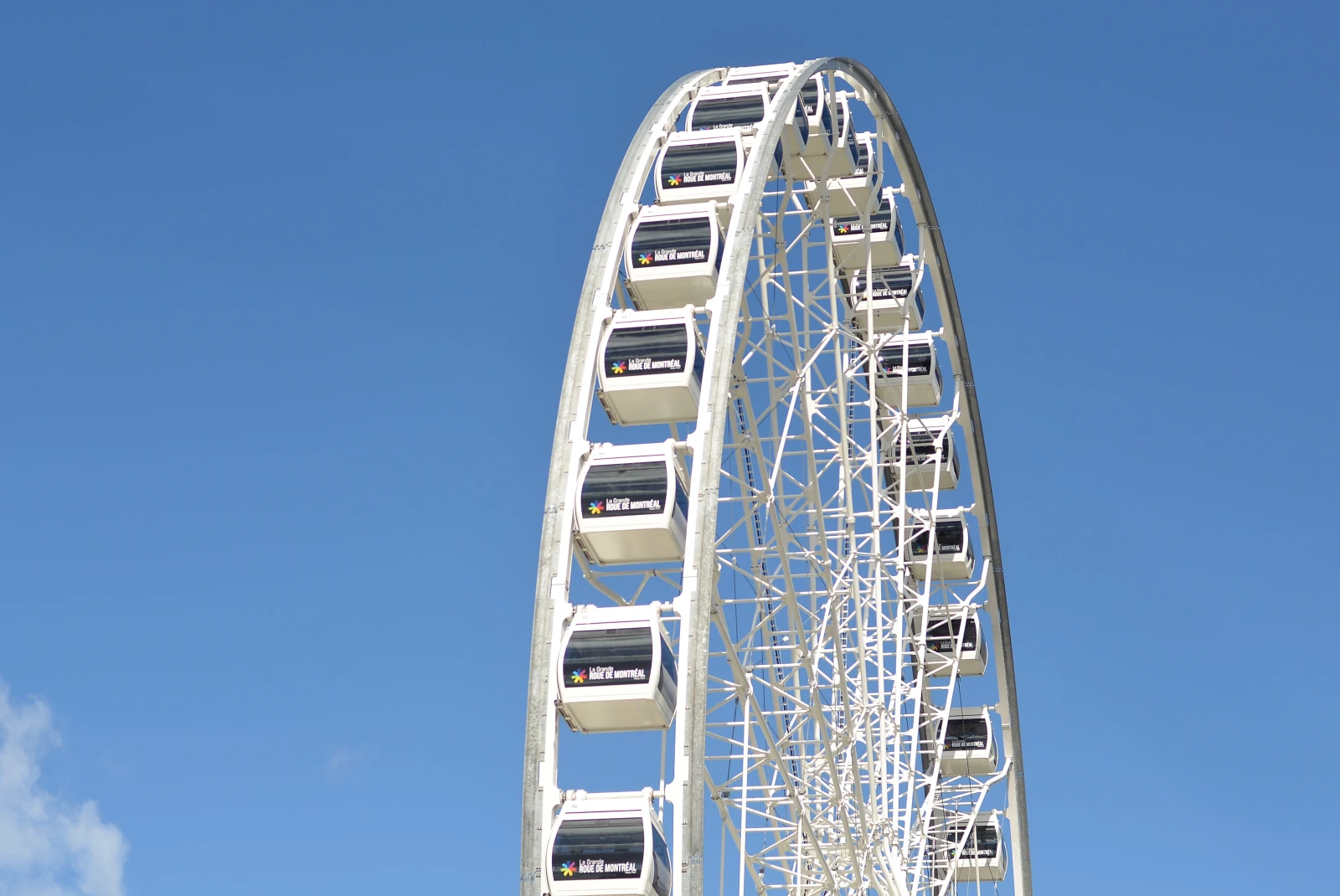 Giant white ferris wheel with dozens of cars with black windows along the double sides wheel with a blue sky backdrop