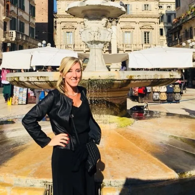 Kathleen Tamburino in a black outfit posing in front of a fountain in Verona, Italy.