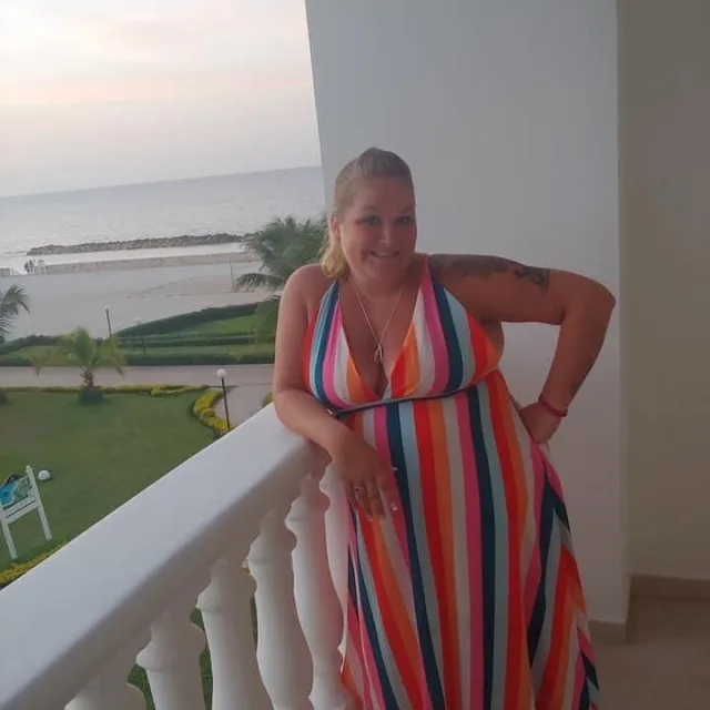 Travel Advisor Tara Pelczar poses on an oceanfront balcony while wearing a colorful, striped dress.