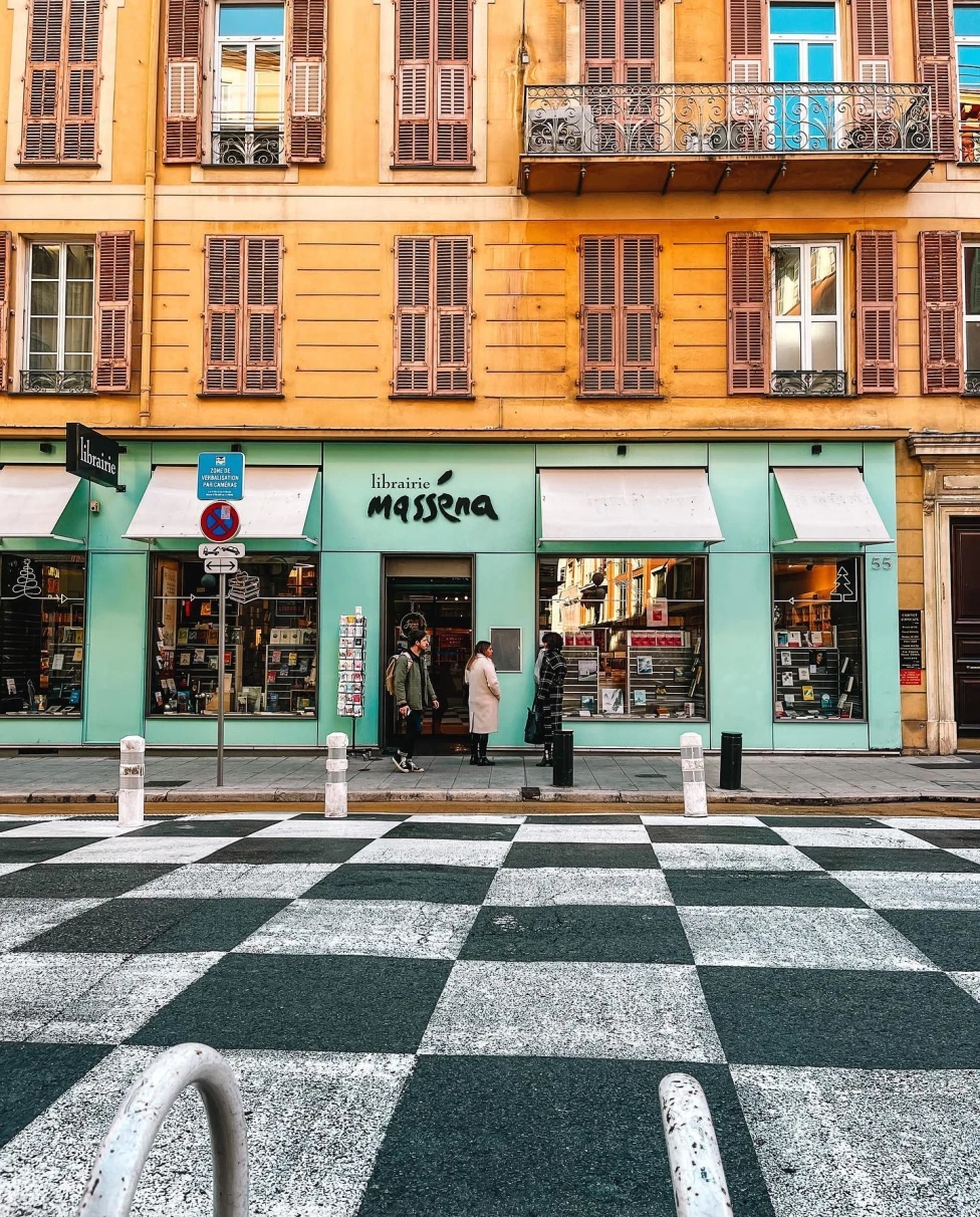 A picture of green and yellow building on a street in the French Riviera. 