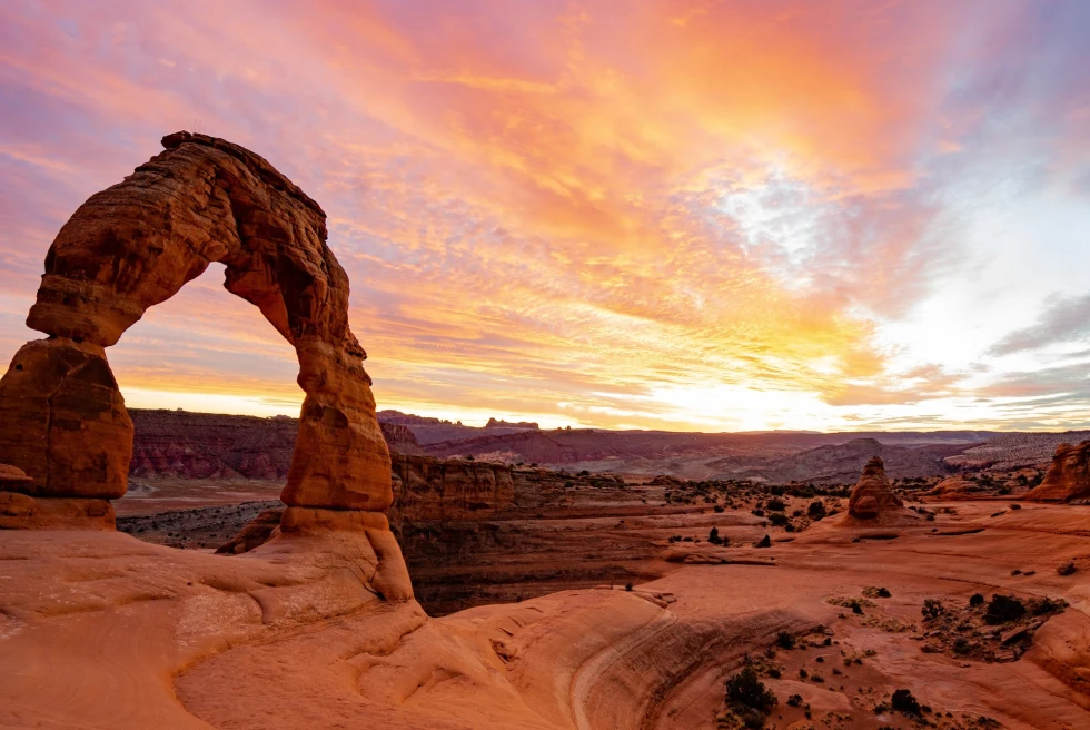a red-rock arch formation against a blue and pink sky at sunset