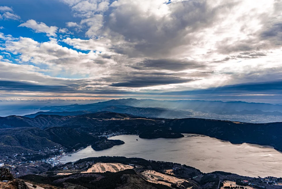 massive lake surrounded by rolling hills of deep green trees with clouded blue sky
