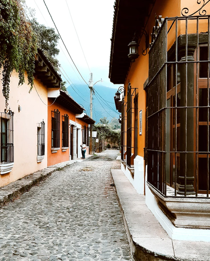 cobblestone streets in Guatemala with green vines and tan orange buildings with a black iron gate