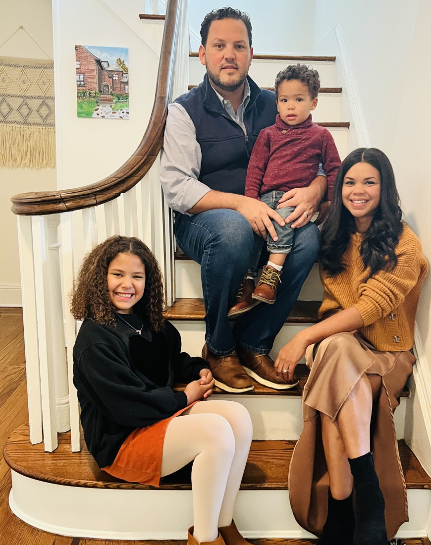 A mother and father sit on a staircase with their two children 