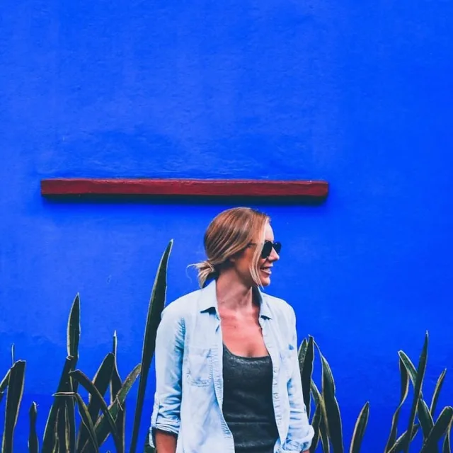 Travel Advisor Mackenzie Bradley in a jean jacket and green shirt in front of a blue wall.