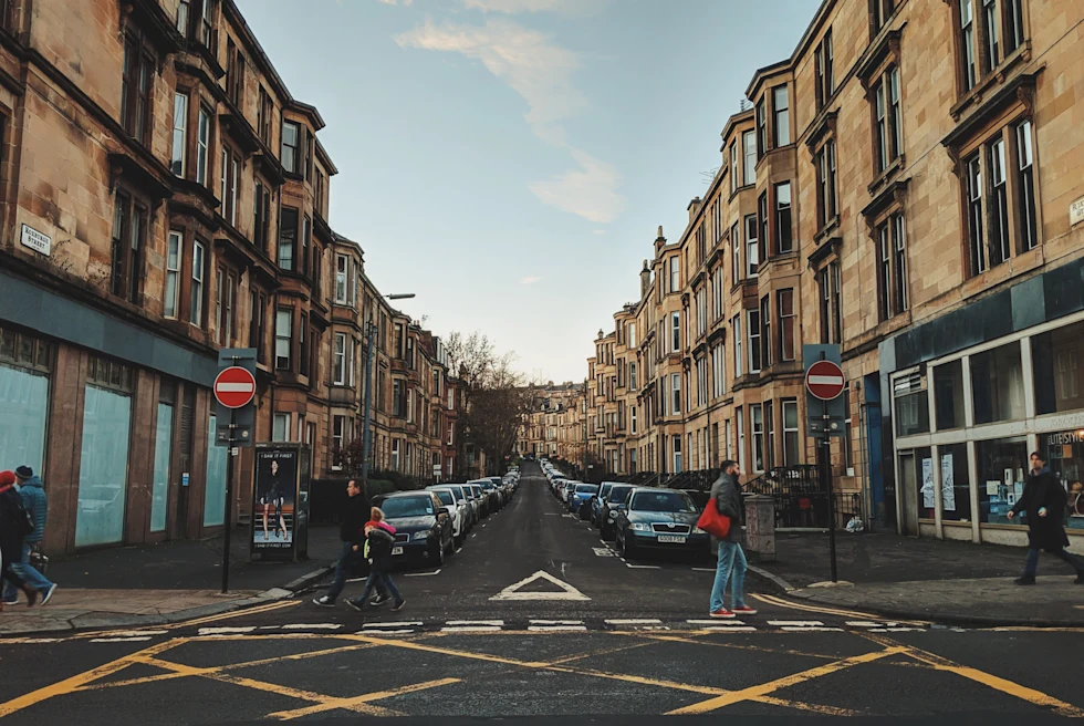 Black asphalt street with yellow and white paint marks and tall yellow buildings with people walking