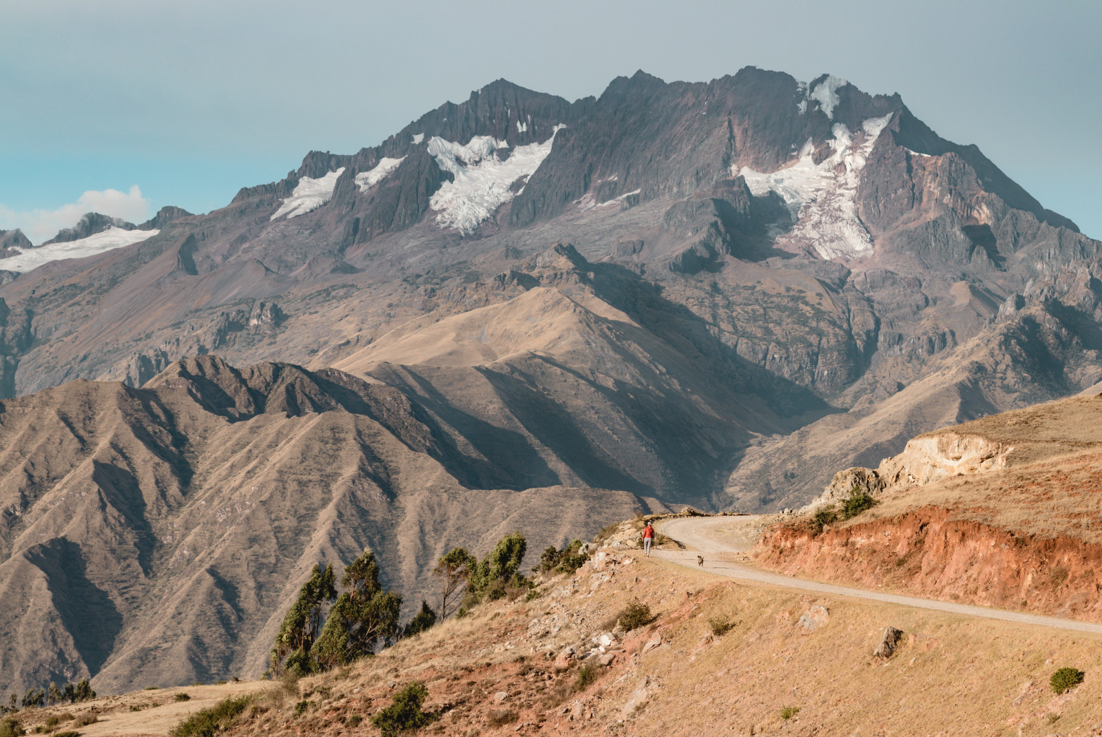 sacred valley in peru tan grass with winding dirt road and brown rocky mountain with snow patches 