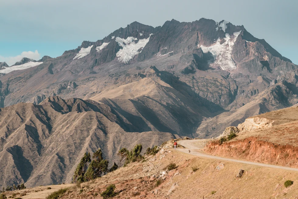 sacred valley in peru tan grass with winding dirt road and brown rocky mountain with snow patches