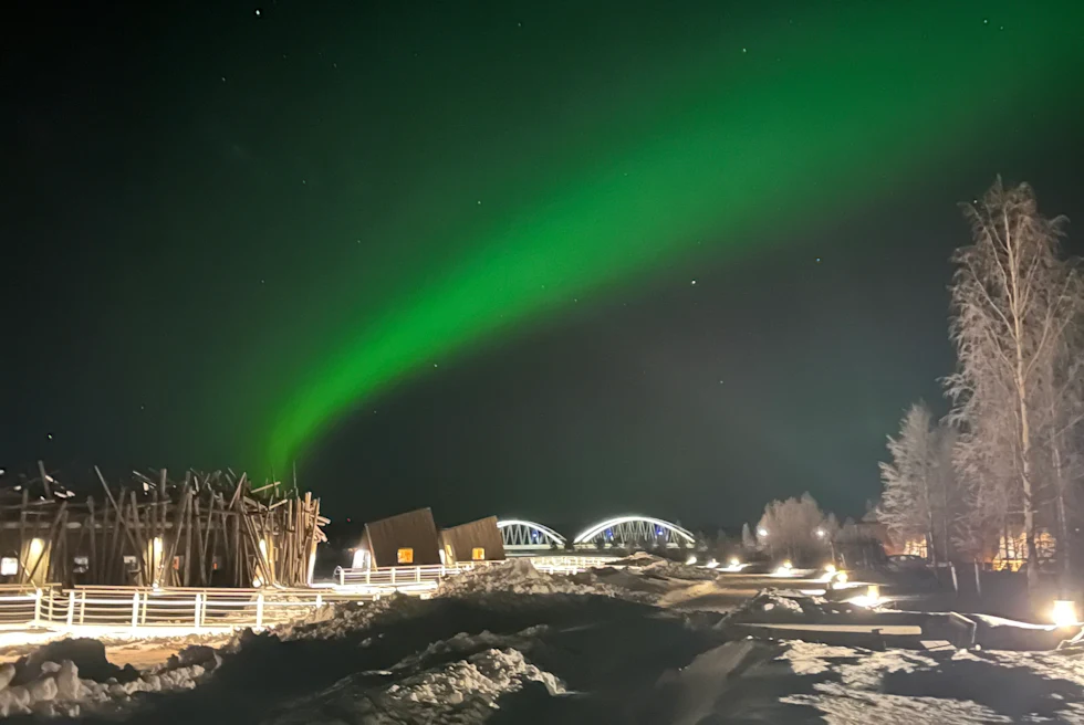 snowy ground with bright green northern lights in the sky