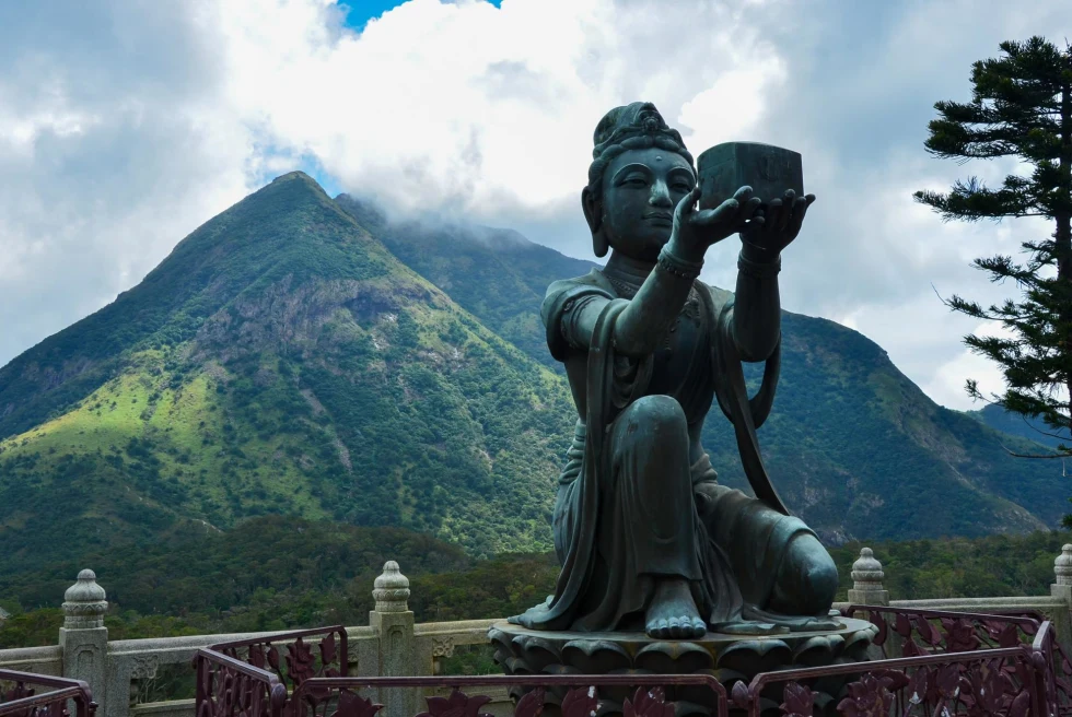 a large Buddha sculpture in front of green mountains shrouded by clouds