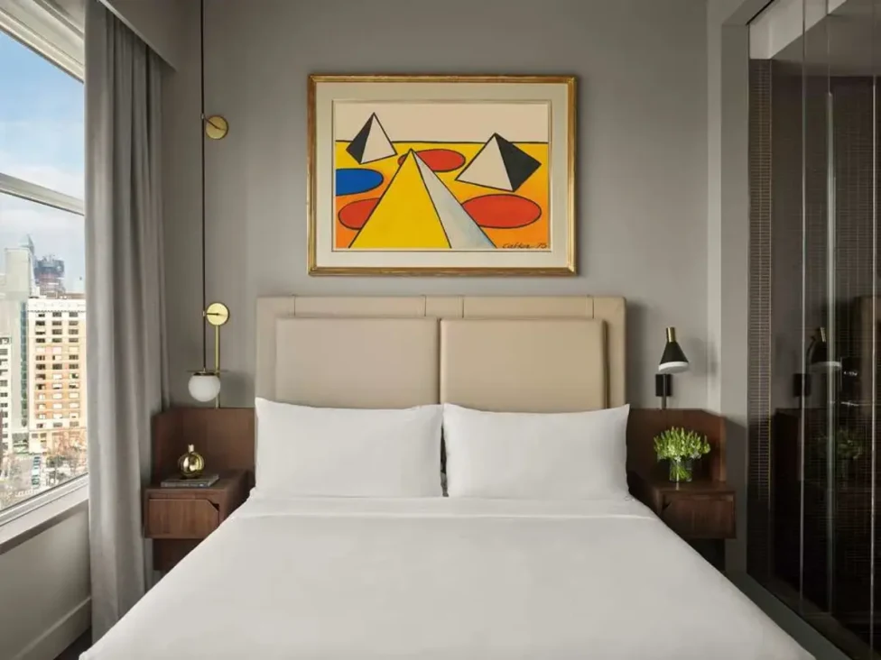 a modern, geometric painting over a white hotel bed