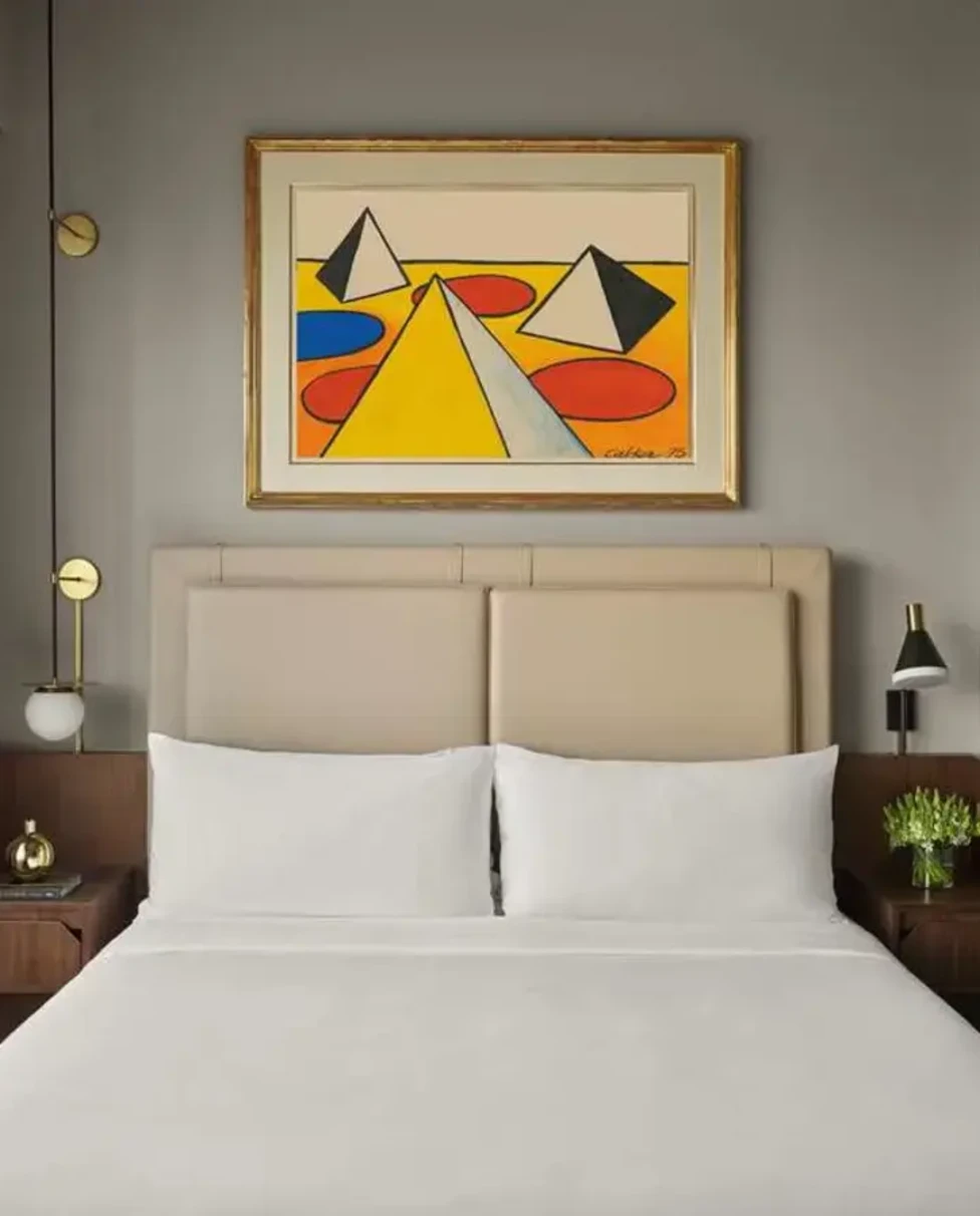 a modern, geometric painting over a white hotel bed