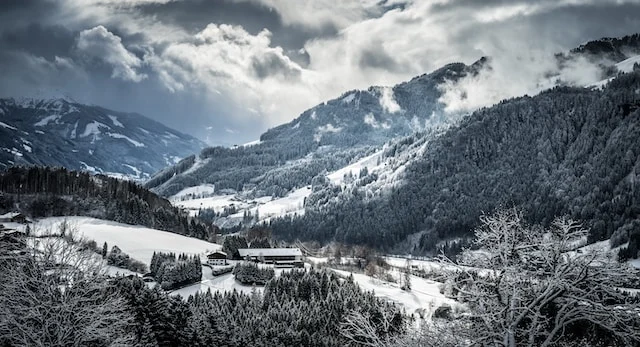 A building in the middle of a snowy valley with tall mountains and trees on either side