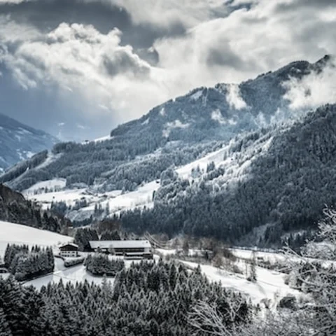 A building in the middle of a snowy valley with tall mountains and trees on either side