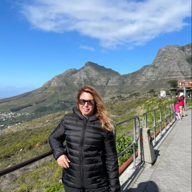 Travel Advisor Leanne Stuhlmiller with a black puffer jacket in front of a green mountain.