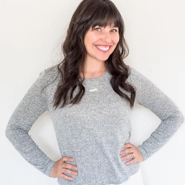 Travel Agent Jenna Rice wearing gray shirt stands in front of white wall