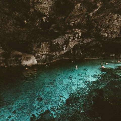 Cenote with natural light flowing through rocks, making the water glow blue.