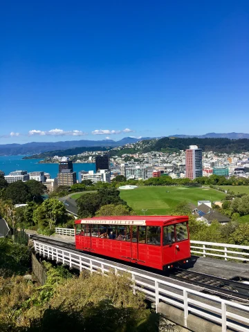 Red bus driving on a bridge with city buildings and sea in the background. 