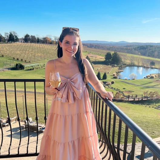 Travel Advisor Amanda Peters in a pink dress holding a wine glass on a balcony overlooking a vineyard.