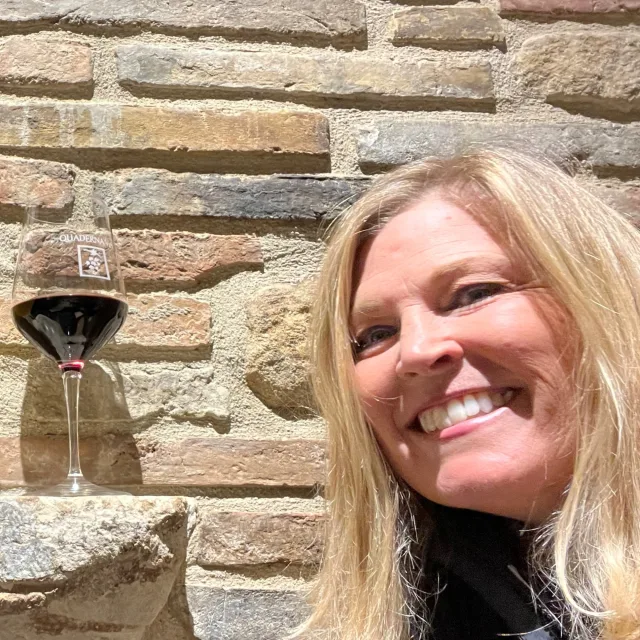 Travel advisor Kelly Mordini with blonde hair smiling in front of a brick wall