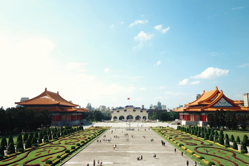 a multi arch structure in the distance with taiwanese traditional buildings at the end of a long mall with green space on either side