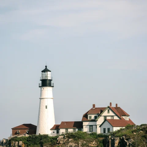 White lighthouse next to house on cliff during daytime
