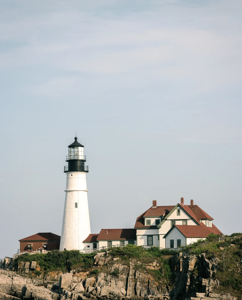 White lighthouse next to house on cliff during daytime