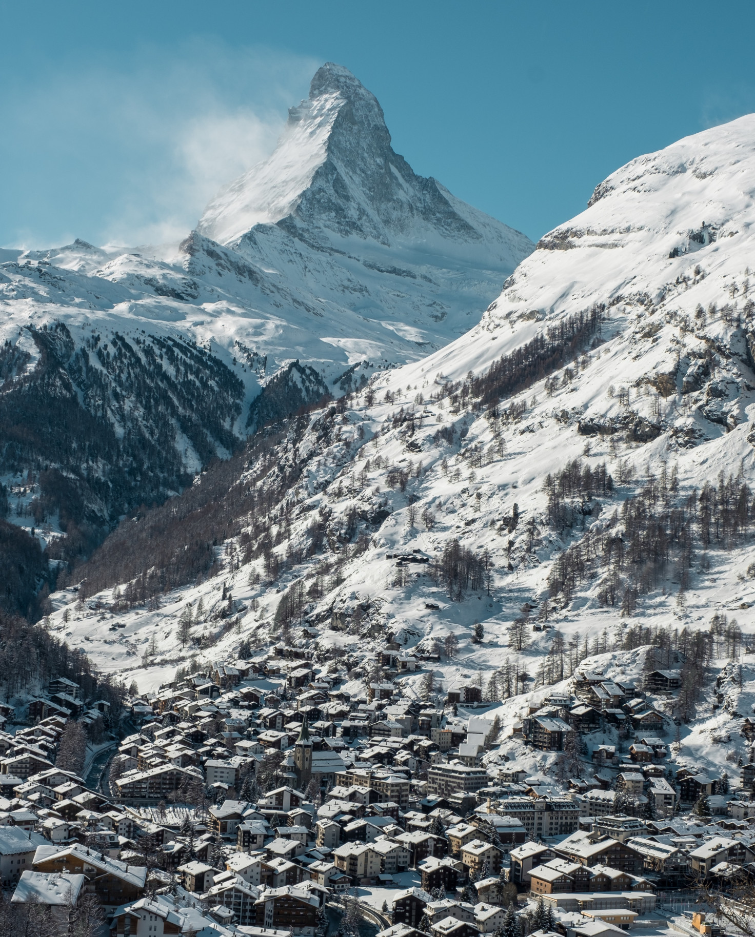 village in a valley surrounded by snowy mountains during daytime