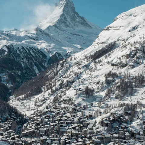 village in a valley surrounded by snowy mountains during daytime