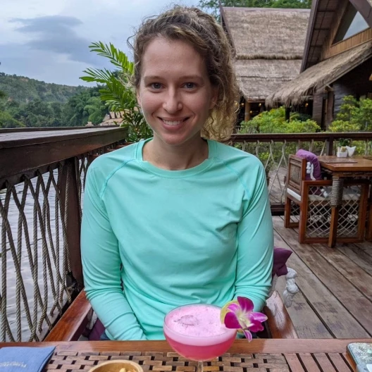 Travel Advisor Robin Schaffer drinking juice on a deck in an aqua shirt. 