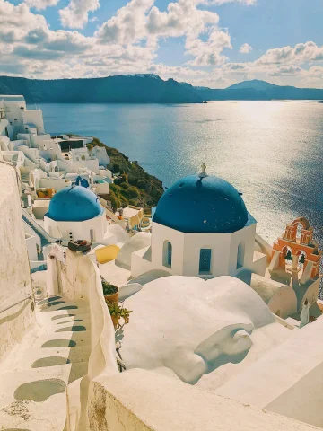 A hillside with white buildings, some with blue dome-shaped roofs, overlooking a beautiful ocean view in Greece