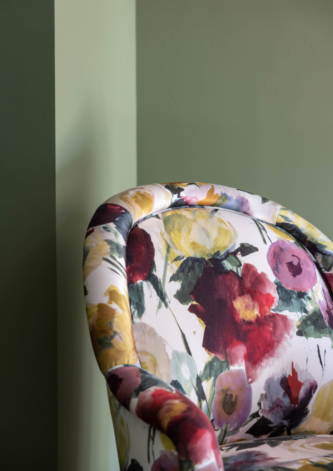 a floral-patterned upholstered chair in front of a green wall